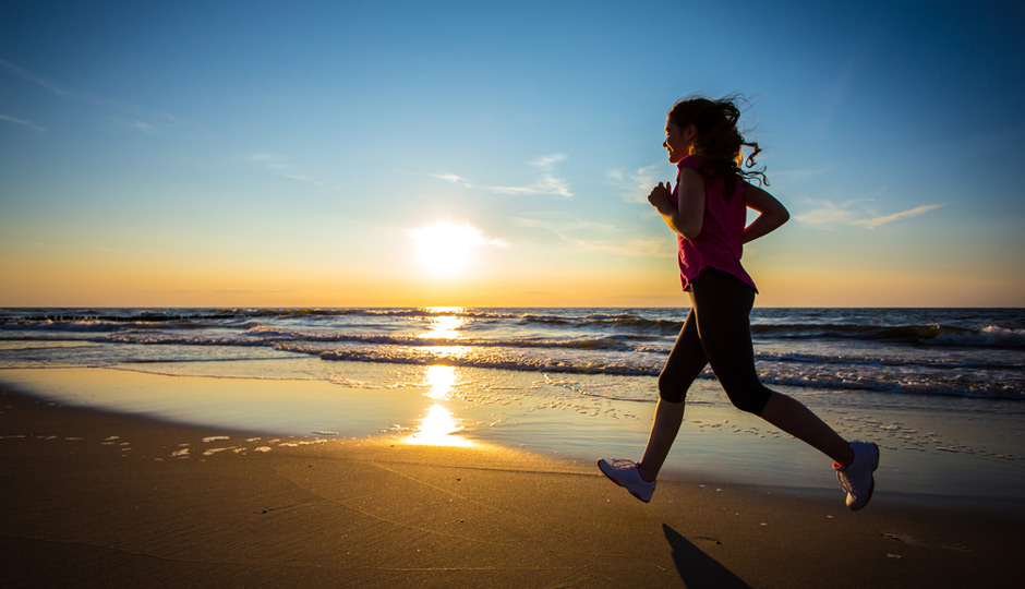 Mulher correndo na praia pôr do sol - morar perto da praia benefícios